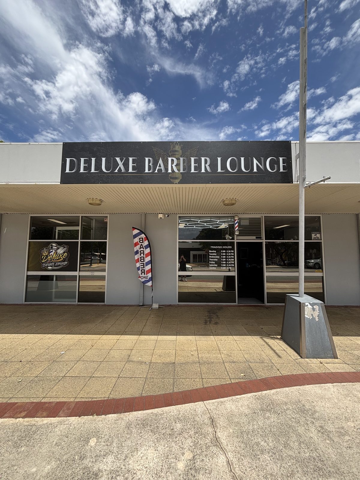The Deluxe Barber Lounge shopfront on Albany Highway, with the black fascia sign and a barber pole flag