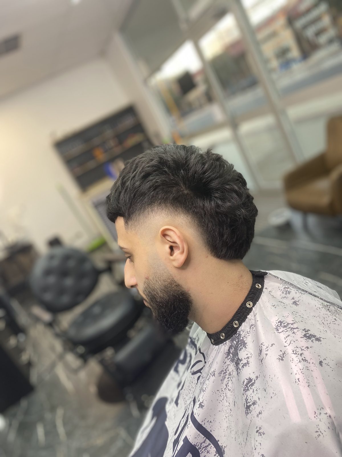 Side view of a finished skin fade with a textured top and a full, shaped beard