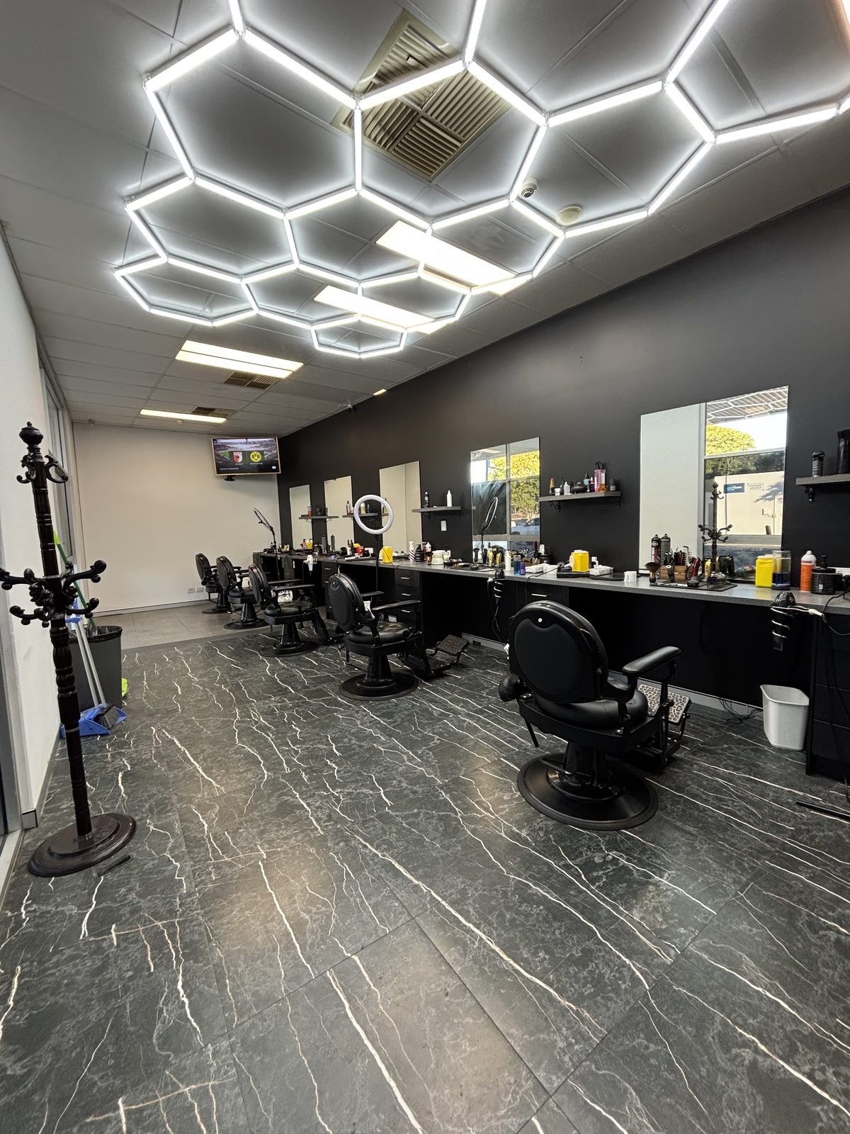 The length of the shop: a row of black barber chairs and mirrors under the hexagon light ceiling